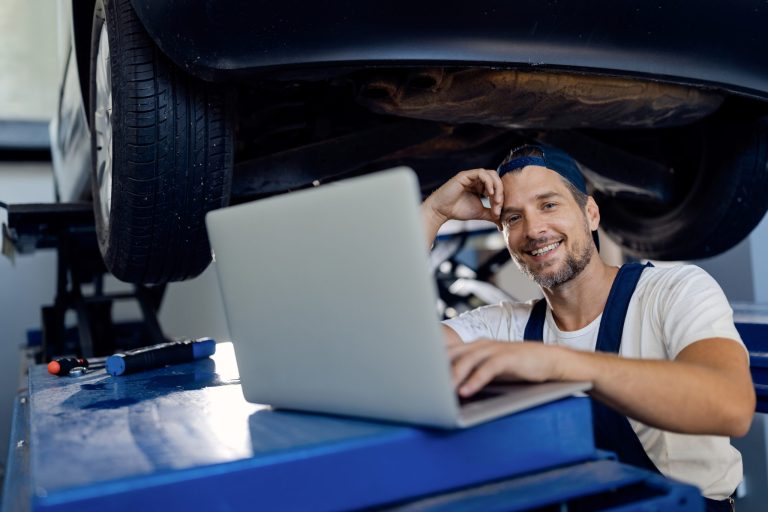 Smiling car mechanic working on the laptop